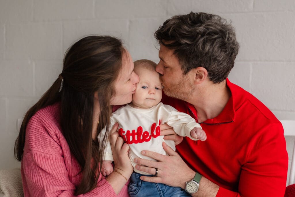 mom and dad kiss baby during valentine's themed 3 month milestone photography session in knoxville tn