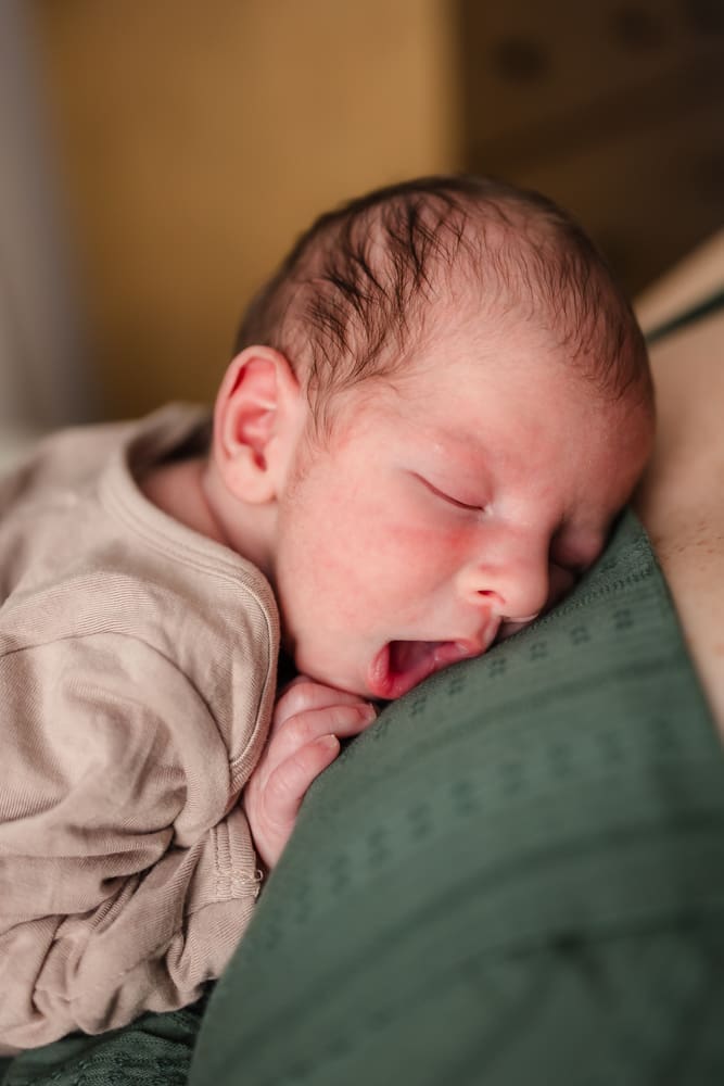 newborn baby boy yawning on mom's chest during in home lifestyle newborn photography session in knoxville tn