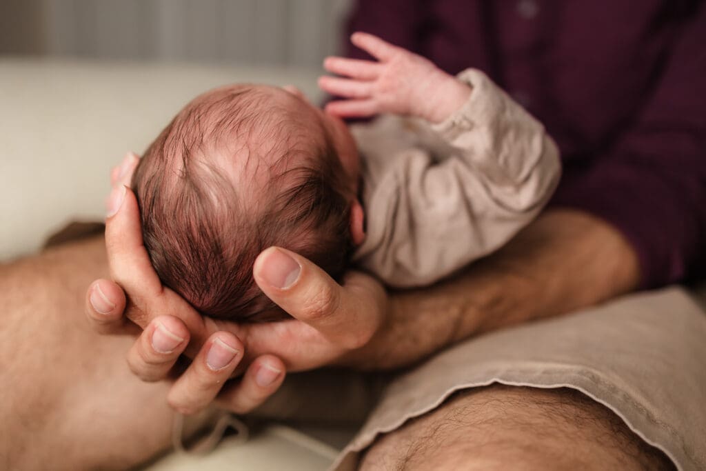 dad's hands on newborn's head during in home lifestyle newborn photography session in knoxville tn