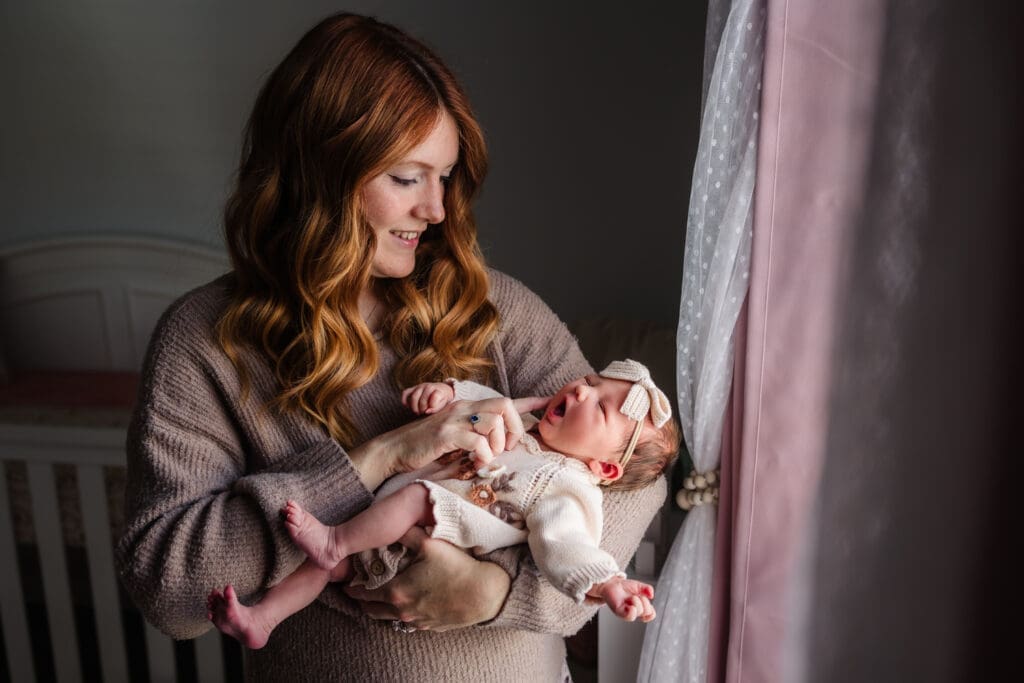 mom holding newborn by window during in-home lifestyle newborn session by knoxville newborn and maternity photographer Kelsey Wood Portraits.