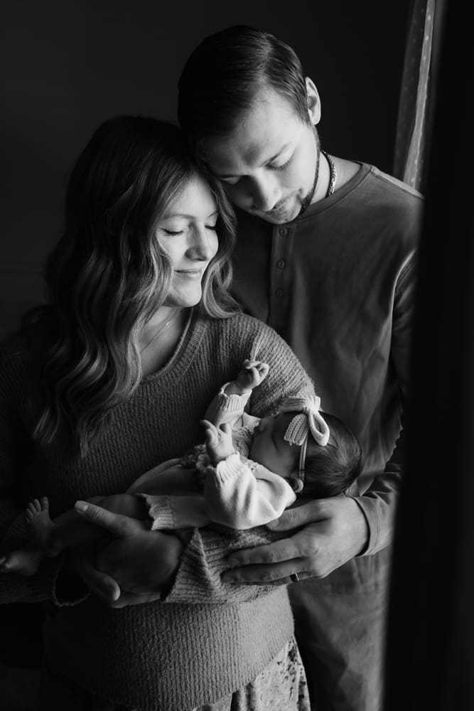 black and white photograph of mom and dad snuggle newborn during in-home lifestyle newborn session by knoxville newborn and maternity photographer Kelsey Wood Portraits.