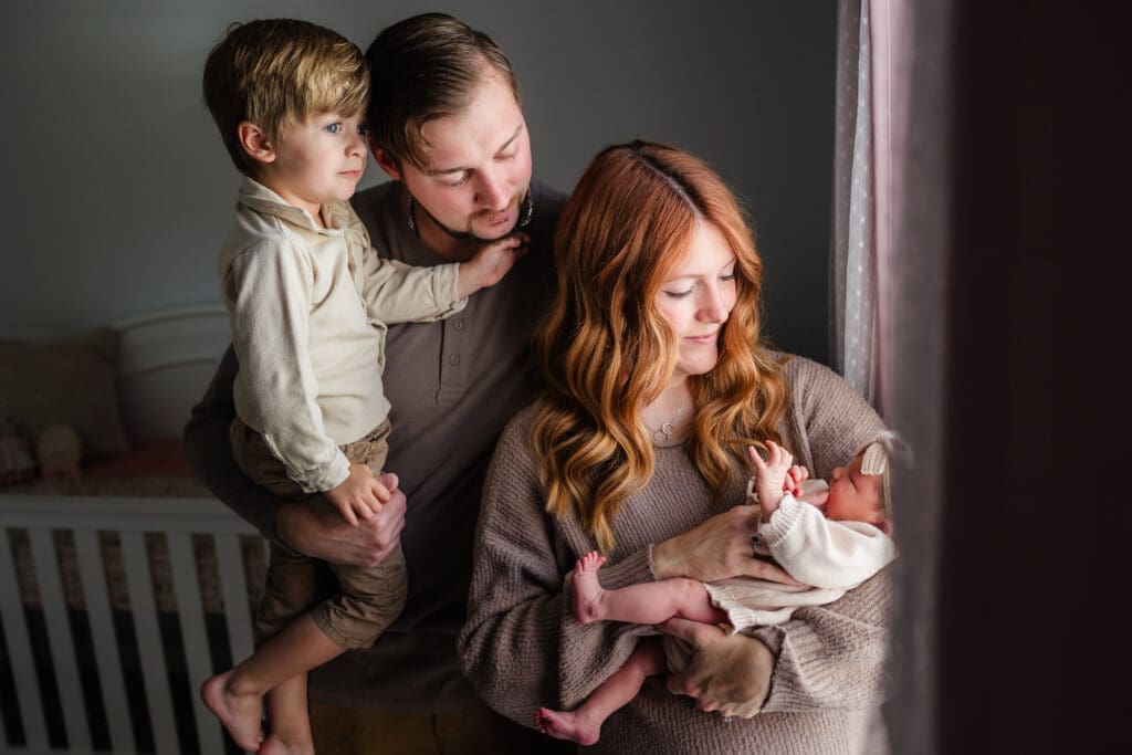 family by window during in-home lifestyle newborn session by knoxville newborn and maternity photographer Kelsey Wood Portraits.