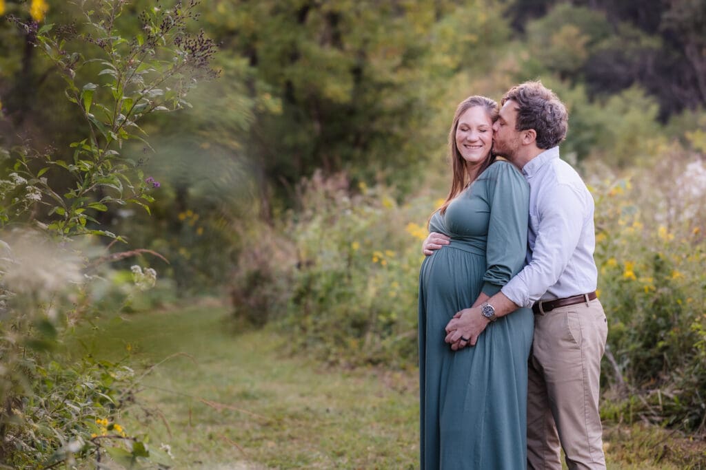 mom and dad snuggling and kissing during knoxville maternity photo shoot at seven isalnds park in kodak