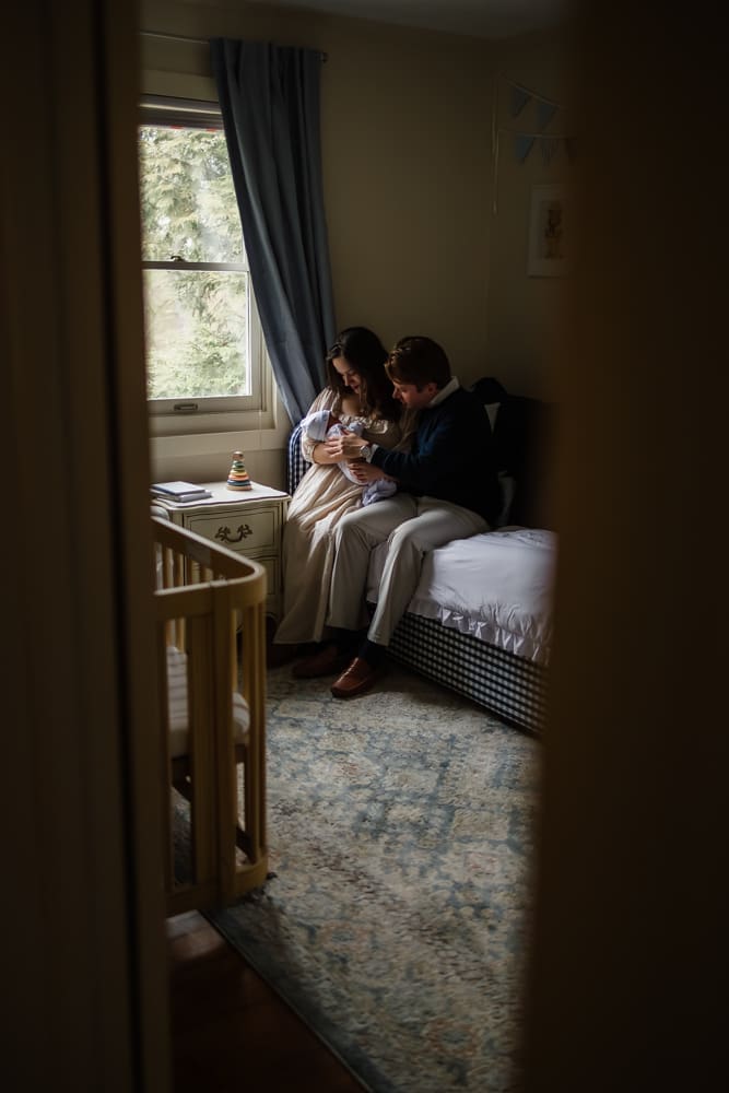 mom and dad admire baby on bed by window during in-home lifestyle newborn photography session in knoxville tn