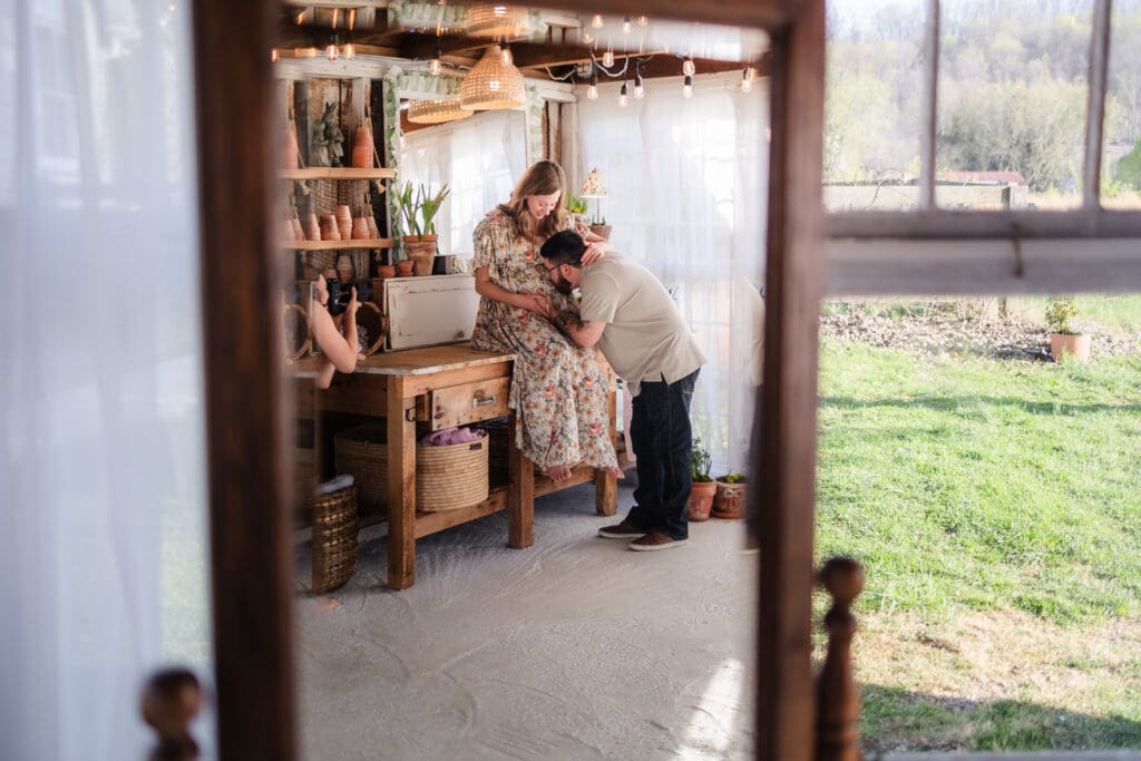 dad kissing baby bump reflection in mirror during knoxville maternity photography session at the Holmstead studio
