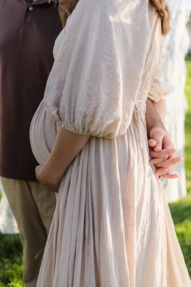 mom and dad holding hands behind moms back during knoxville maternity photography session at the Holmstead studio