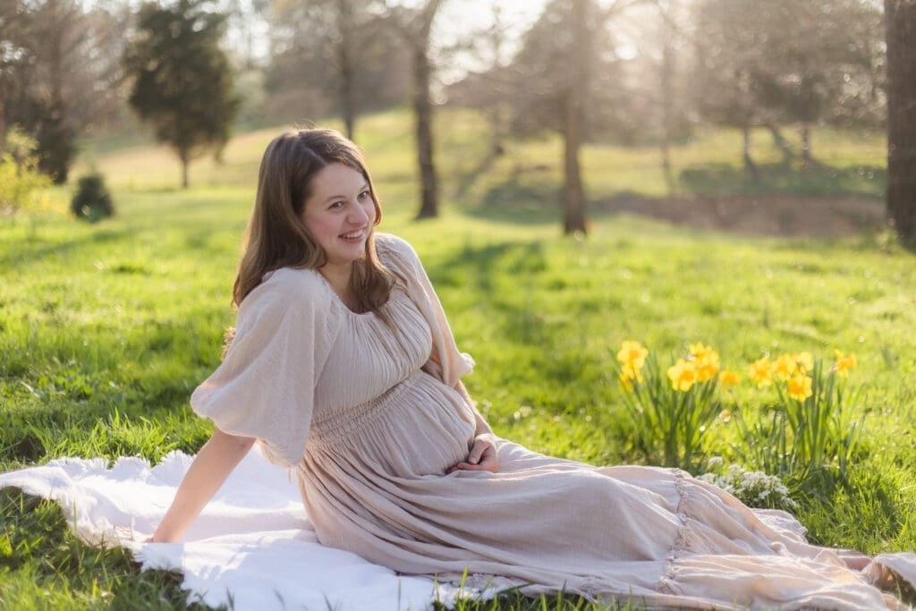 mom holds baby bump sitting on the ground during knoxville maternity photography session at the Holmstead studio
