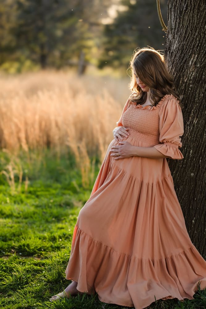 mom leaning on tree rubbing baby bump during knoxville maternity photography session at the Holmstead studio