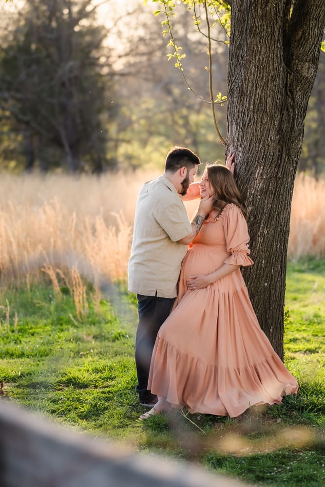mom and dad having a moment leaning on tree during knoxville maternity photography session at the Holmstead studio
