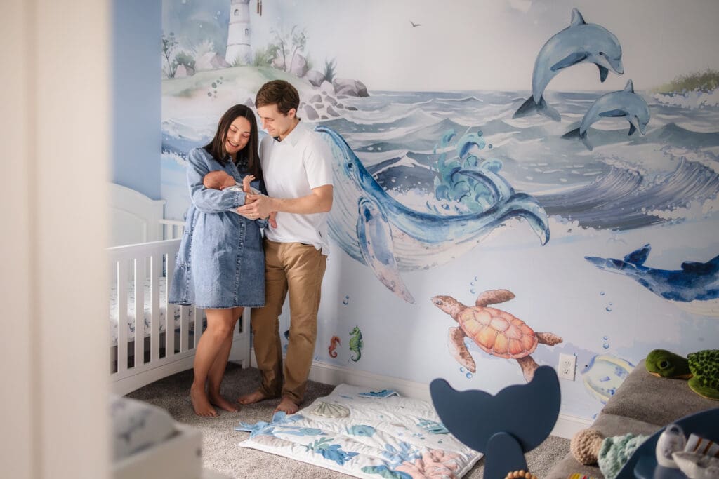 mom and dad standing in ocean themed nursery admiring newborn boy during knoxville in-home lifestyle newborn photography session
