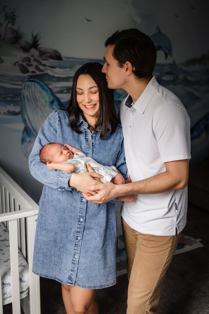mom looking at newborn baby and dad kissing mom in ocean themed nursery during knoxville in-home lifestyle newborn photography session
