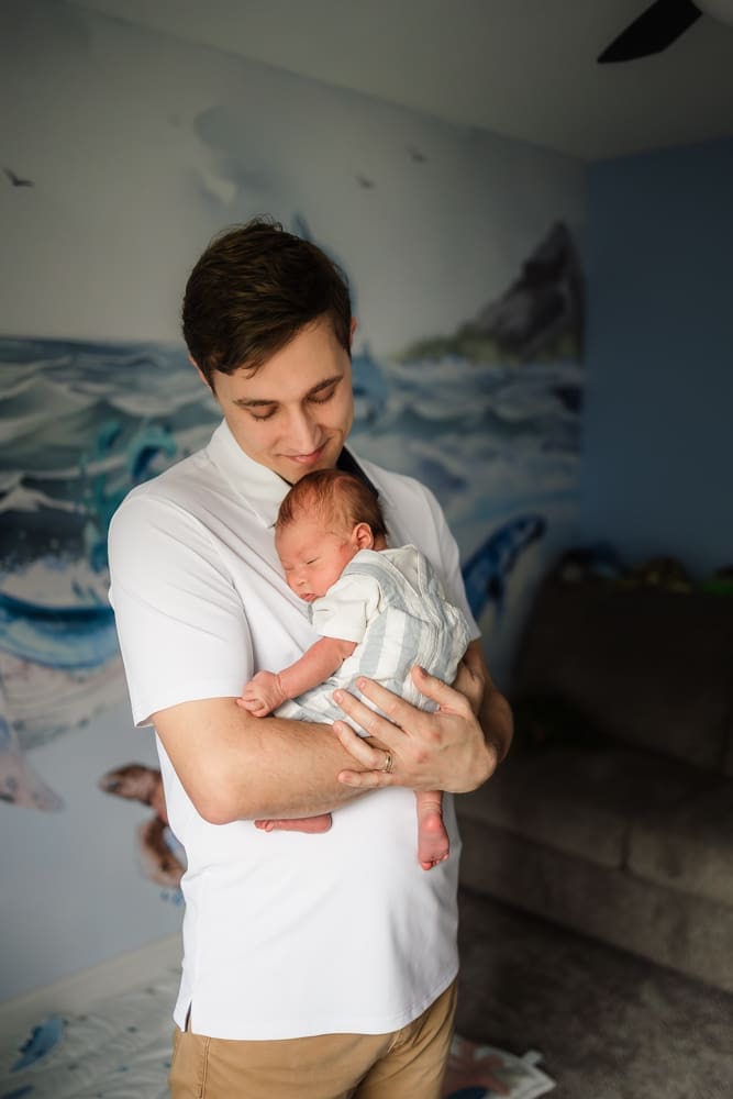 dad looking at sleeping newborn son in ocean themed nursery during knoxville in-home lifestyle newborn photography session
