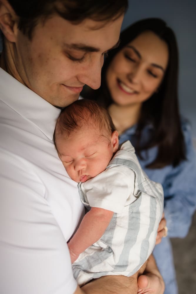 baby boy sleeping on dad's chest while mom watches smiling during knoxville in-home lifestyle newborn photography session