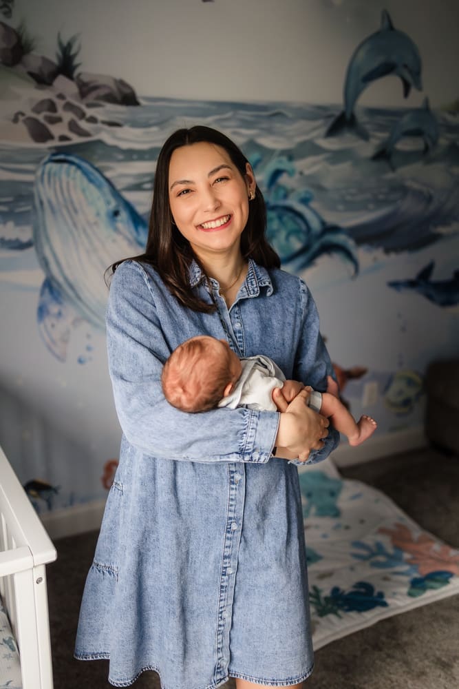 mom smiling and holding newborn son during knoxville in-home lifestyle newborn photography session