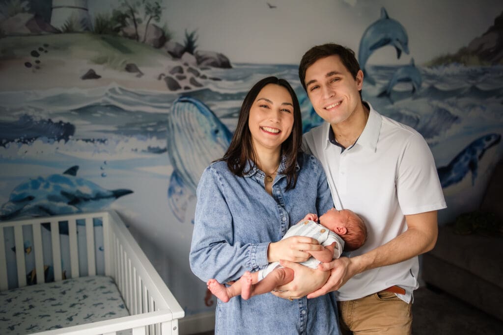 mom and dad smiling at camera holding newborn during knoxville in-home lifestyle newborn photography session