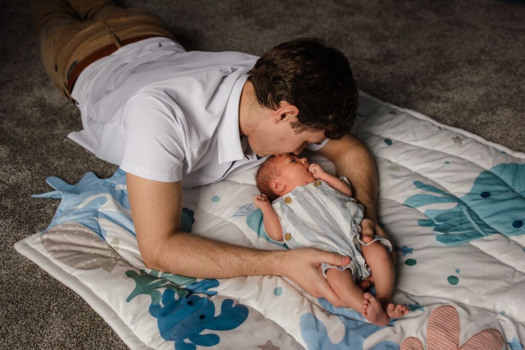 dad laying on floor with newborn kissing son during knoxville in-home lifestyle newborn photography session