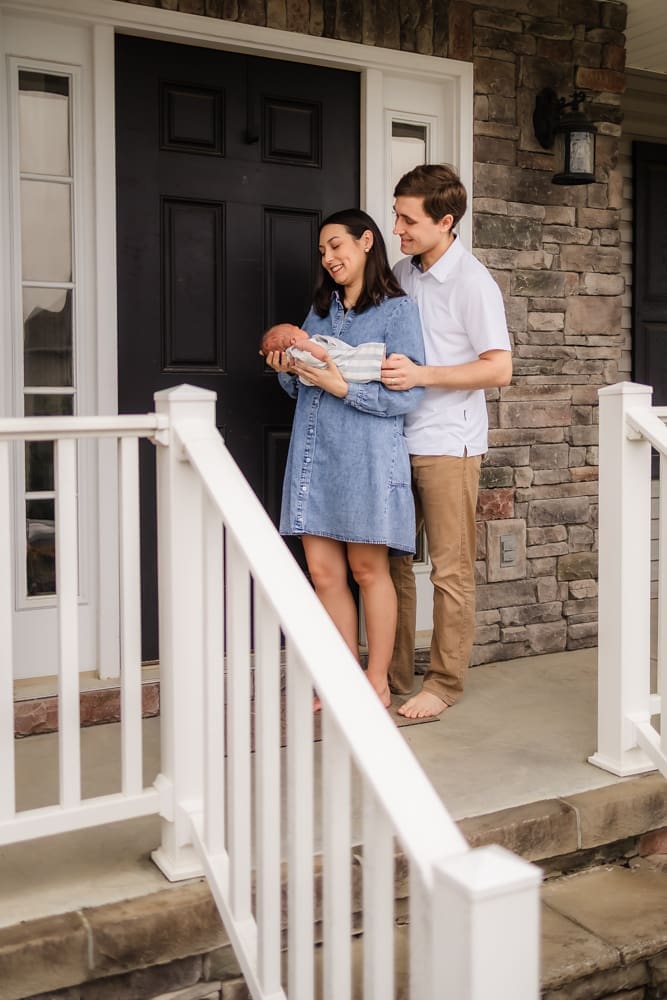 mom and dad on front porch holding newborn during knoxville in-home lifestyle newborn photography session