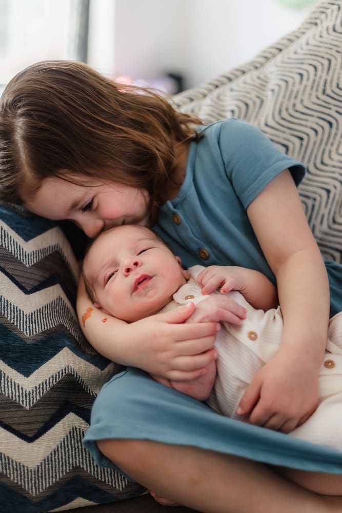 big sister kissing newborn brother during in-home newborn session