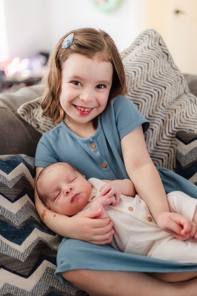 big sister smiling and holding newborn brother during knoxville lifestyle newborn session