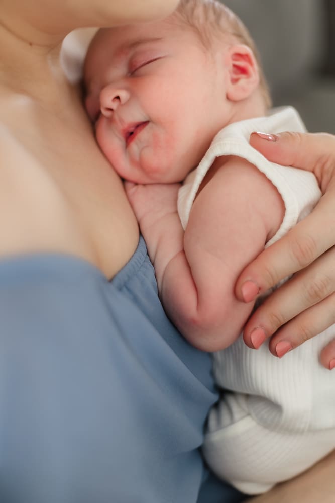 baby boy smiles and snuggles into moms chest during newborn photoshoot in-home