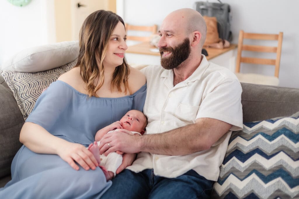 mom and dad smile at each other while holding baby during newborn photos