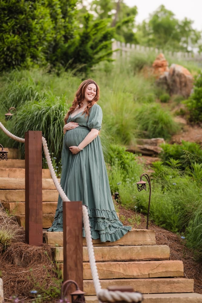 mom posing in olive green dress on stairs during fantasy inspired knoxville maternity photography session at ancient lore village