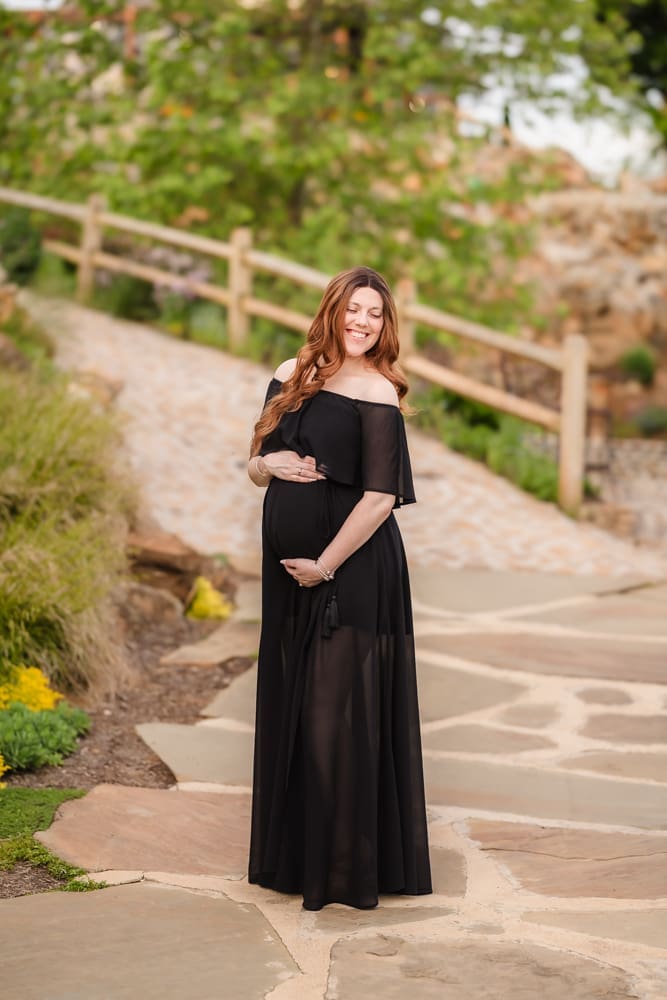 mom smiling at baby bump in black dress during fantasy inspired knoxville maternity photography session at ancient lore village