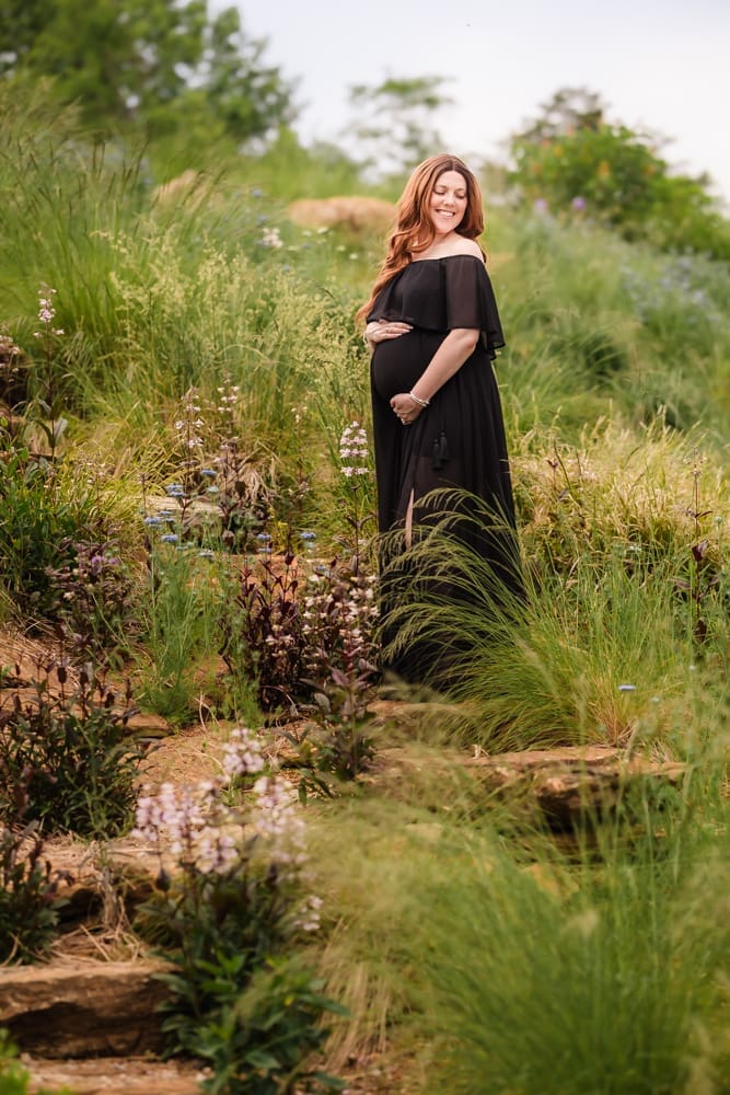 mom standing in grass and flowers during fantasy inspired knoxville maternity photography session at ancient lore village