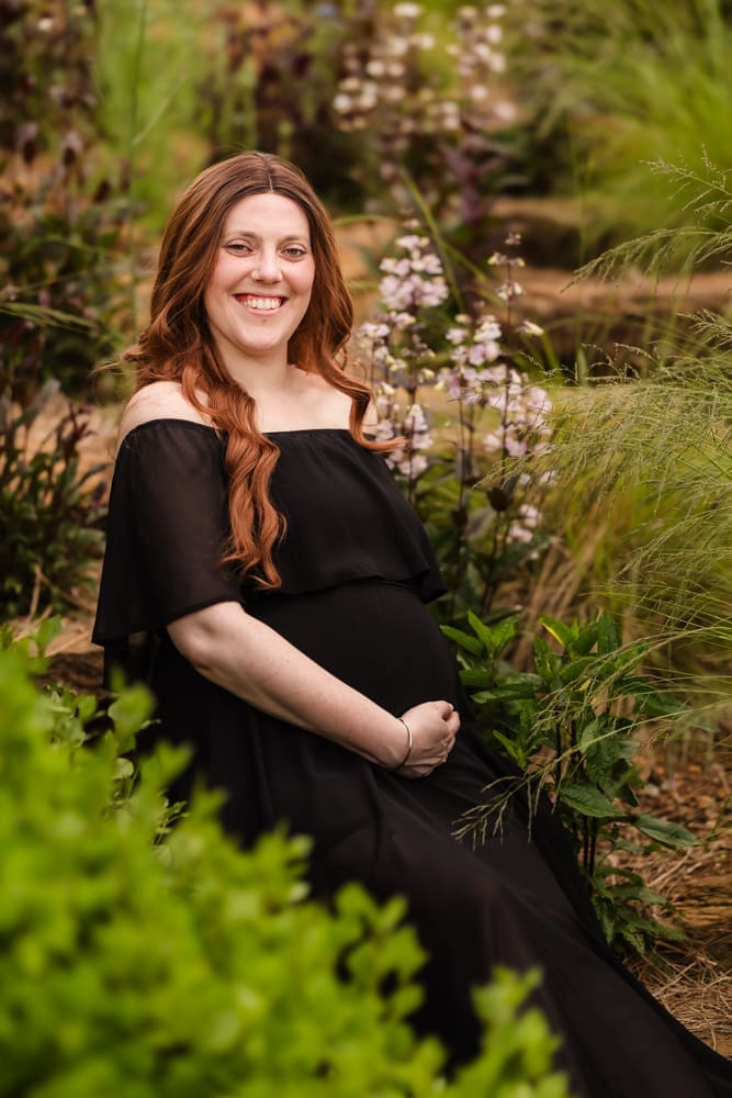 mom sitting among flowers during fantasy inspired knoxville maternity photography session at ancient lore village