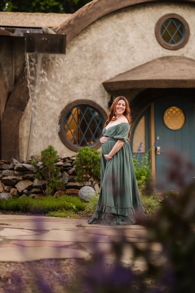 mom holding baby bump in front of cottage during fantasy inspired knoxville maternity photography session at ancient lore village