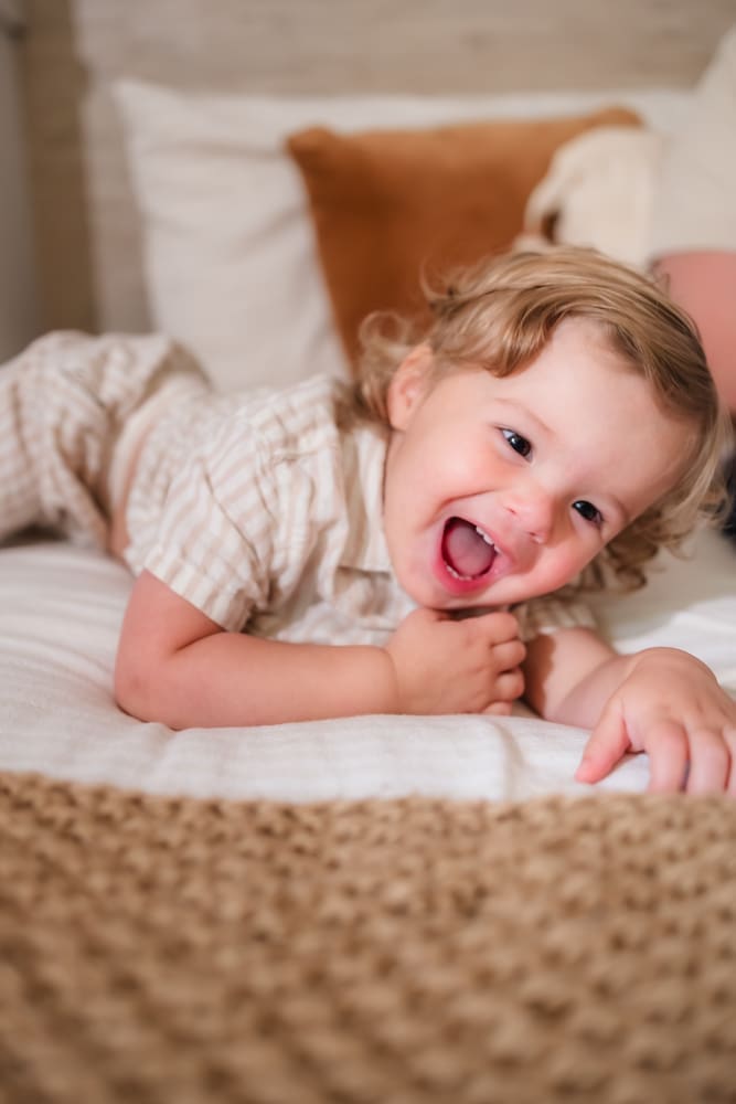 Toddler brother smiling on the bed during an in-home newborn session in Powell TN