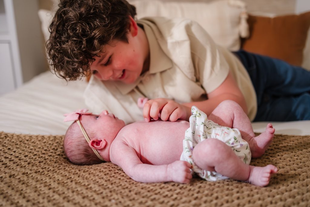 Big brother gently interacting with his newborn sister during in-home newborn photography in Powell TN