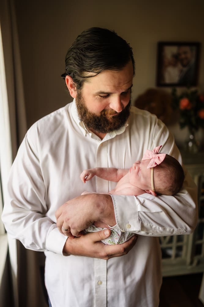 Father holding his newborn daughter beside a window during a Powell TN newborn session